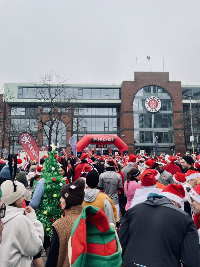 Im Vordergrund stehen viele weihnachtlich verkleidete Läufer, im Hintergrund sieht man das Millerntorstadion